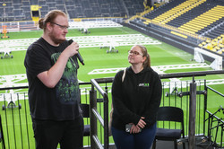 Die zwei Vertreter*innen des AstA halten eine Rede. Im Hintergrund das Fußballfeld und die leeren Tribünen des BVB-Stadions.