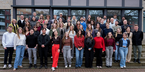 Eine große Gruppe von Personen steht für ein Gruppenfoto vor einem Gebäude auf einer Treppe.