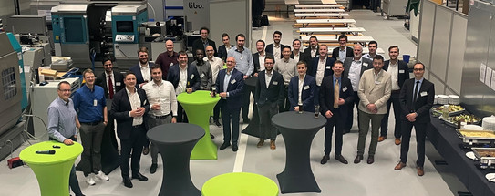 Kick-off event In a large room with many machines stands a large group of men and smiles at the camera