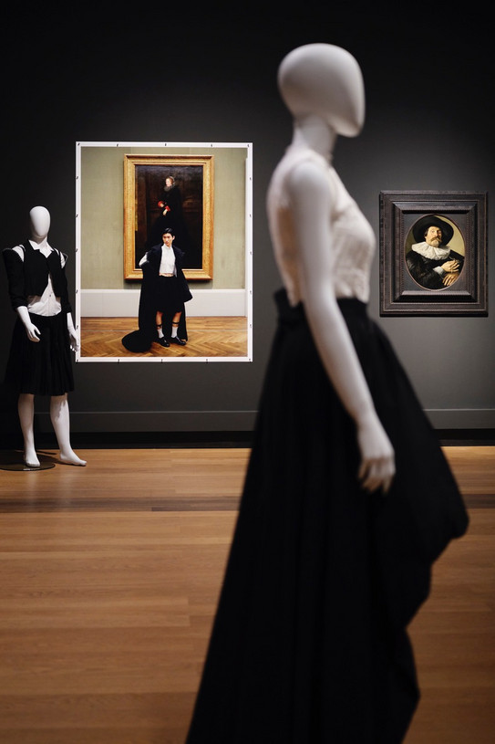 Ein Blick in die Ausstellung mit Schaufensterpuppen, die aktuelle Mode tragen, sowie einer Fotoarbeit und einem Gemälde im Hintergrund.