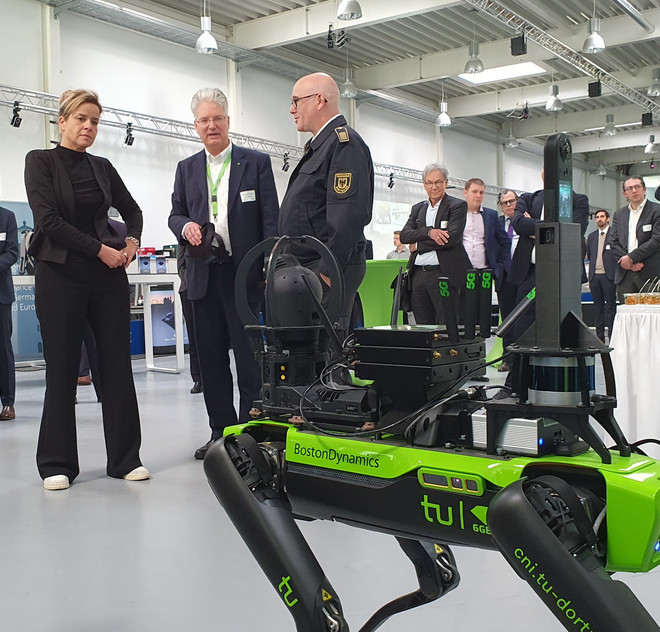 Mona Neubaur, Prof. Wietfeld und Dirk Aschenbrenner von der Feuerwehr Dortmund und dem Deutschen Rettungsrobotikzentrum unterhalten sich und schauen auf ein roboterhundähnliches Exponat.