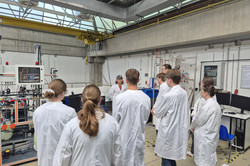 Veranstaltung "Chemieanlagen und Computer?!" Teilnehmende stehen mit einem Kittel und einer Schutzbrille in einer Halle mit Chemieanlagen.
