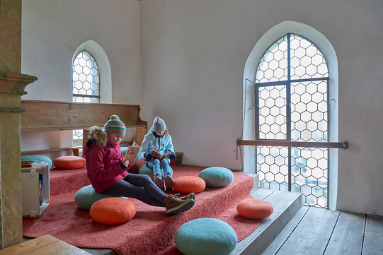 Auf dem Foto sieht man zwei Mädchen, die in der Leseecke der Kirche lesen.