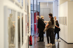 Im Zentrum des Bildes sind Besucher*innen der Ausstellung zu sehen, die sich Bilder anschauen.