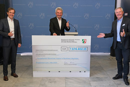 Drei Männer in Anzügen stehen mit etwas Abstand lächelnd nebeneinander.