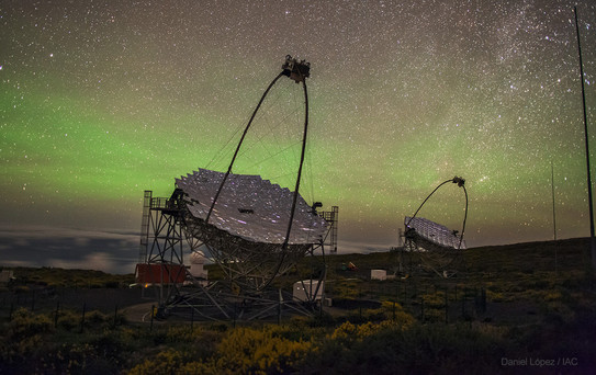 Zwei große, hochmoderne Teleskope stehen versetzt hintereinander auf einer grasigen Fläche. Im Hintergrund ist ein sternenreicher Nachthimmel zu sehen.