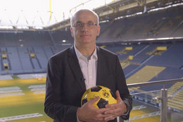 Rektor Prof. Bayer steht im BVB-Stadion und hält einen Ball in der Hand.