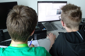 Zwei Teilnehmer entwickeln am PC einen Quellcode. 