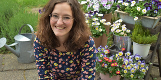 Marlene Schlüter Eine junge Frau sitzt lächelnd in einem Garten.