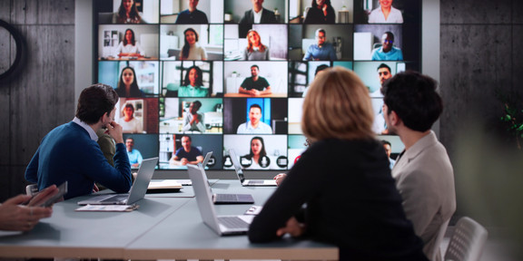 Vier Menschen an einem Tisch, die an einer Videokonferenz teilnehmen