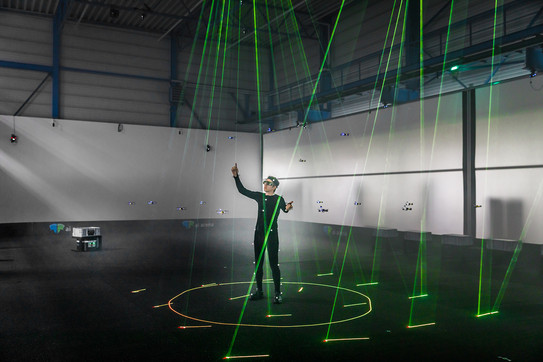 Ein Mann, der in einem großen Raum steht. Auf ihn sind viele grüne Laser gerichtet.