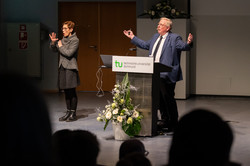 Genzel gesticulates at the speaker's podium, an interpreter translates into sign language