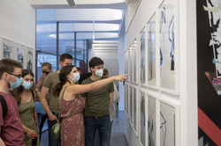 Mehrere Personen stehen an einer weißen Wand an der Bilder einer Kunstausstellung hängen.