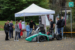 Mehrere Personen stehen in und um ein Pavillon-Zelt, das auf dem Campus der TU Dortmund aufgestellt wurde. Vor dem Pavillon steht ein kleiner Rennwagen.