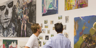 Zwei Menschen stehen vor einer Wand mit Bildern.