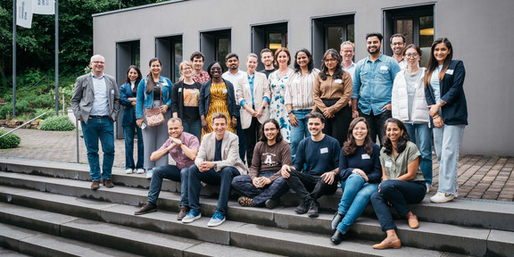 Gruppenfoto auf einer grauen Treppe. Im Hintergrund ein kleines, graues Gebäude der RUB.