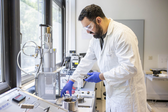 Mr. Nicolás Gajardo-Parra stands in the laboratory wearing protective clothing. In front of him are some apparatuses.