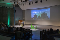 Fully seated Audimax with a view of the stage, a telescope is shown in the presentation