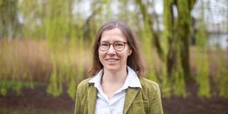 Ein Porträtfoto von einer Frau mit Brille und weißer Bluse auf dem Campus der TU Dortmund.