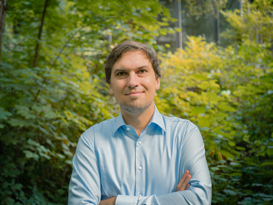 Porträtfoto von Christian Glaser: Prof. Glaser trägt ein hellblaues Hemd und hat die Arme verschränkt. Im Hintergrund sind Büsche.