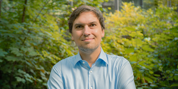 Porträtfoto von Christian Glaser: Prof. Glaser trägt ein hellblaues Hemd und hat die Arme verschränkt. Im Hintergrund sind Büsche.