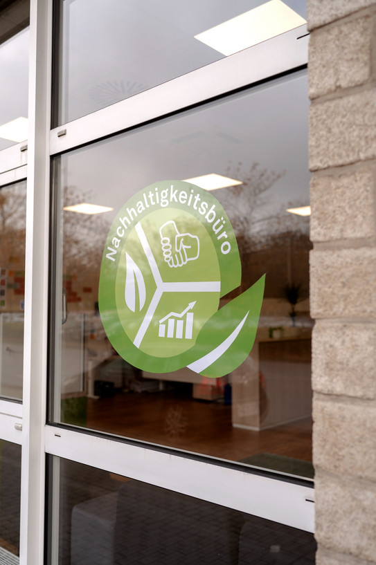 An einer Fensterscheibe klebt das grün-weiße Logo des Nachhaltigkeitsbüros der TU Dortmund.