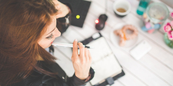 A woman is sitting at a desk with a pen in her mouth.