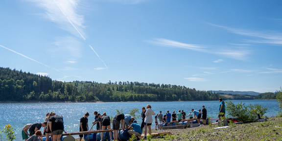 Trainees are on the shore of a lake building a raft together.