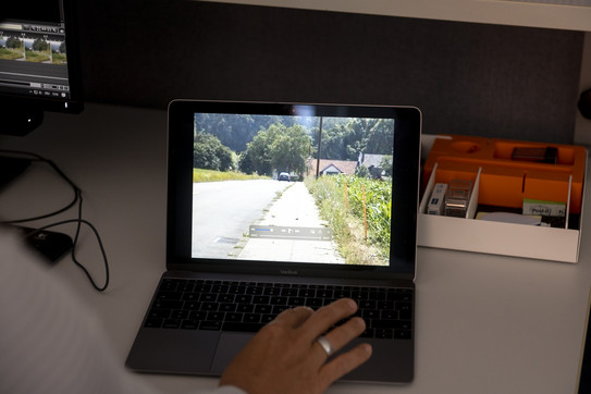 Ein Laptop-Bildschirm zeigt ein Video von einer Landstraße, auf der Tastatur liegt eine Hand.  