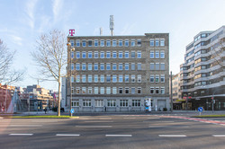 Exterior view of an office building with a Telekom logo on the roof on a street. Next to it other city buildings.