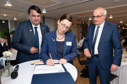 20 Jahre New York Büro - Unterzeichnung Im Zentrum des Bildes sind die drei Rektor*innen der UA Ruhr. Prof. Barbara Albert steht an einem Stehtisch in der Mitte des Bildes und unterschreibt ein Dokument.