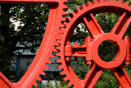 Zahnräder Campus Nord Die Zähne von zwei großen roten Zahnrädern aus Stahl verhaken sich.