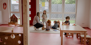 HoKiDo-Anbau 3 Eine Gruppe von Kindern spielt mit einer Erzieherin auf dem Boden.