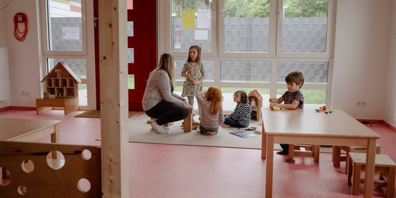 HoKiDo-Anbau 3 Eine Gruppe von Kindern spielt mit einer Erzieherin auf dem Boden.