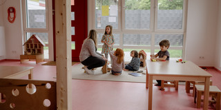 Eine Gruppe von Kindern spielt mit einer Erzieherin auf dem Boden.