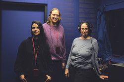Foto: Drei Personen stehen mit Kopfhörern in einem Tonstudio neben einem Mischpult.