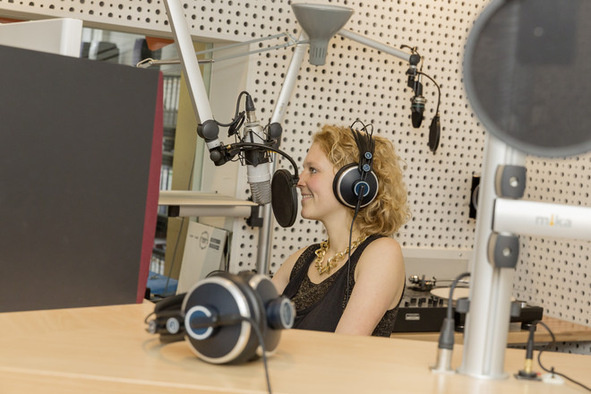 Studentin lächelt am Mikrofon bei der Aufnahme im Studio von Eldoradio