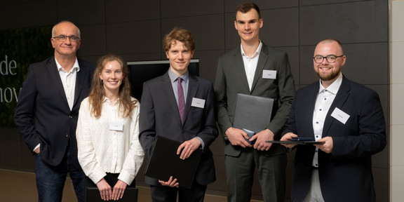 Foto: Fünf Personen stehen nebeneinander und halten Urkundenmappen in den Händen.