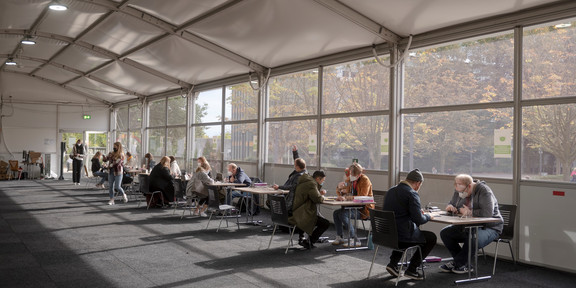 In a tent, people sit at several counters to check the proofs.