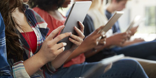 Das Bild zeigt mehrere Schüler*innen, die auf ein Tablet in ihren Händen schauen