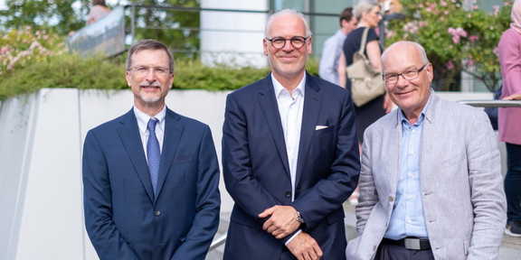 Three men in suits pose side by side for a photo.