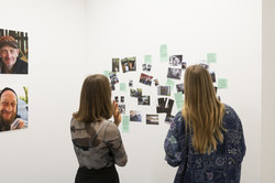 Zwei Besucherinnen betrachten eine Installation aus Fotos und Texten.