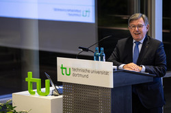 A man in a suit with a blue tie stands at the lectern.