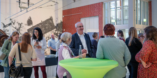 Bei einer Auftaktveranstaltung stehen viele Personen in einer Halle und unterhalten sich.