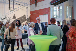 Juni Bei einer Auftaktveranstaltung stehen viele Personen in einer Halle und unterhalten sich.