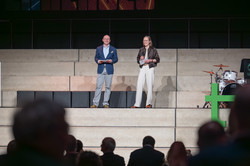 Foto: Zwei Personen moderieren gemeinsam auf einer Bühne.