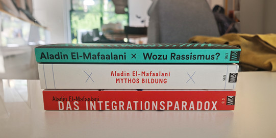 Drei Bücher, die übereinander gestapelt auf einem Tisch liegen.