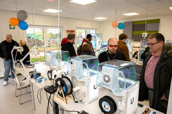 The picture shows two rows of tables, each with three identical-looking devices and visitors looking at them.
