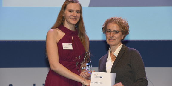 A young woman in a red dress receives a certificate on a stage.