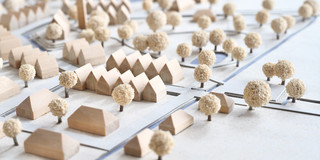 Ein Stadtmodell aus kleinen hölzernen Häusern und Bäumen auf weißem Grund
